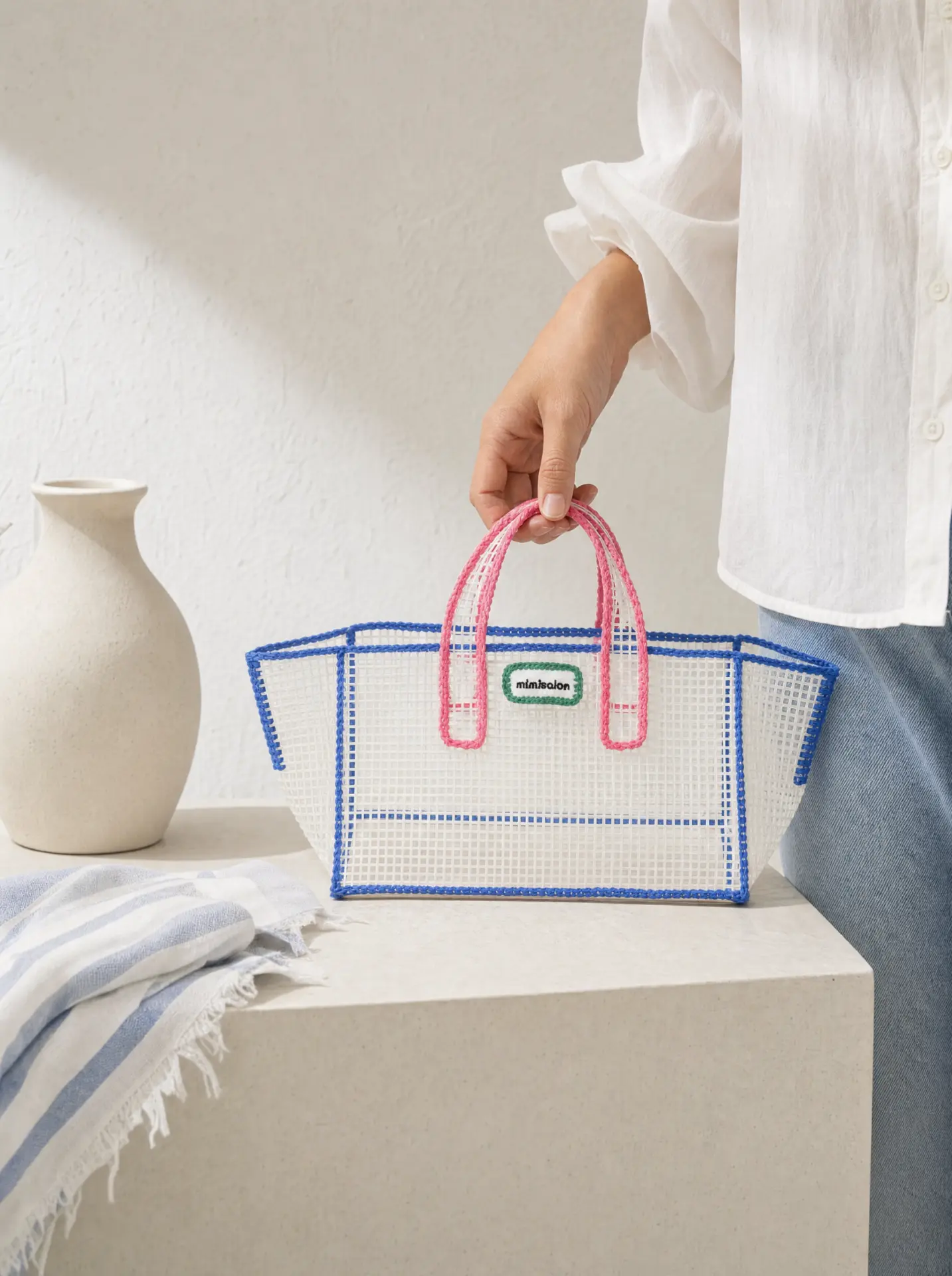 White mesh tote with blue trim and pink handles on a plaster plinth